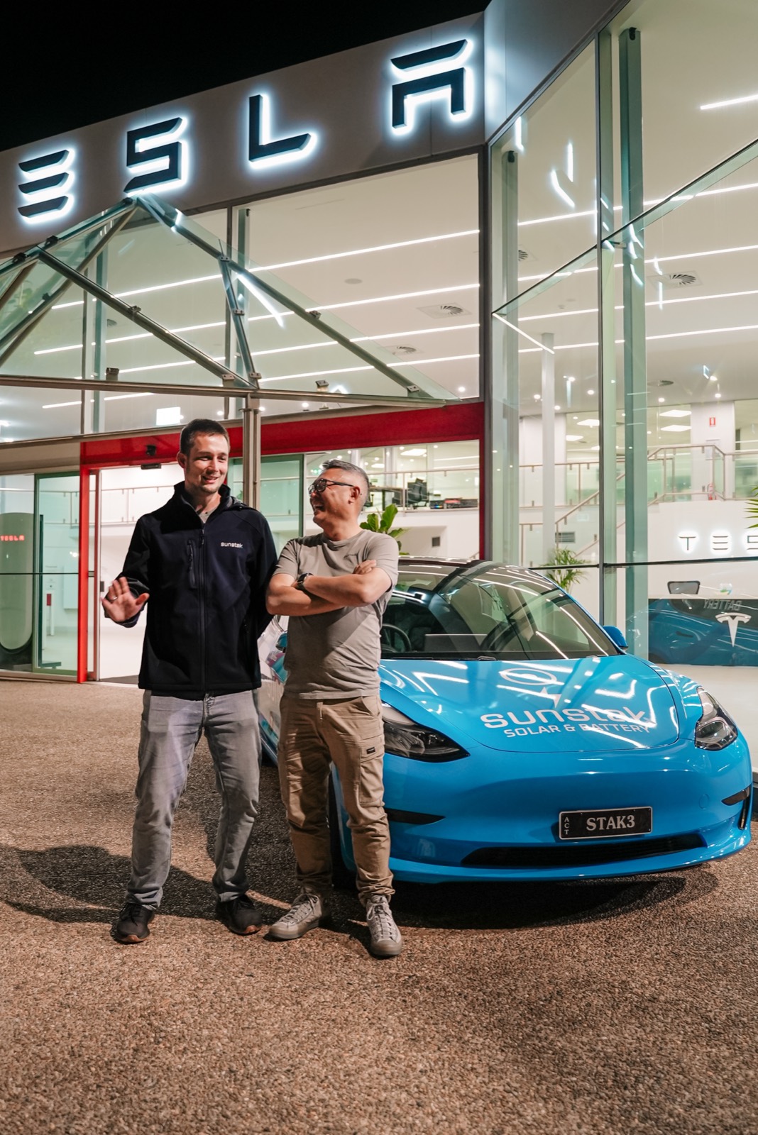 Two guests beside the blue Sunstak Tesla at night